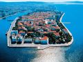 
W Chorwacji, tuż nad brzegami Morza Adriatyckiego leży Zadar - piękne miasto, idealnie dostosowane do potrzeb turystyki. Jest to jedno z ulubionych miast dalmackich, wybierane na spędzenie odprężającego urlopu, a to ze względu na liczne okoliczne atrakcje, jak i dopisującą ciągle pogodę. 

Historia 

Początki Zadaru sięgają najdawniejszych wieków, a do czasów współczesnych wciąż na jego terenie zachowało się mnóstwo niemych świadków starożytnych wydarzeń. Miasto jest położone w historycznej krainie, Dalmacji (niegdyś Iliria, Illyricum). Na terenie dawnej Dalmacji wpływ swój zaznaczyli Grecy, przypływając tu już w VIII w. p.n.e. W II w. p.n.e. kraina dostała się w ręce Rzymian, którzy uczynili z niej swoją prowincję - Illyricum. To właśnie z tego obszaru pochodziło trzech sławnych cesarzy, którzy są odpowiedzialni za restaurację Rzymskiego Cesarstwa - Klaudiusz II, Aurelian oraz Dioklecjan. 
W czasach rzymskich Zadar został doceniony, co przełożyło się na szybki rozwój miasta. Typowy plan, z uwzględnieniem charakterystycznego dla starożytnego świata rzymskiego forum, zachował się po dzień dzisiejszy. 
Po upadku Cesarstwa Rzymskiego, Dalmacja stała się obszarem należącym do Bizancjium. Od VI wieku zaczęły tu swój wpływ zaznaczać plemiona słowiańskie. W VII wieku Słowianie stali się poważnym zagrożeniem dla władzy bizantyjskiej -z trudem obronił się przed nimi Konstantynopol. Nie udało się to natomiast Dalmacji, gdzie jedynie nieliczne miasta zachowały swą niepodległość. W tym Zadar. Kolejna wielka próba dla niezależności przyszła wraz z kolejnymi wiekami. Po długich rywalizacjach, Chorwacja zyskała własnych królów. Starali się oni rozszerzyć swoją władzę na całą chorwacką Dalmację. Budziło to sprzeciw miast tego obszaru. Autonomiczny pozostał wciąż Zadar, który wysunął się na pierwsze miejsce, stając się siedzibą bizantyjskiego stratega. W kolejnym czasie bizantyjskie miasta w Chorwacji zaczęły podejmować stosunki handlowe ze Słowianami, co przyniesie ze sobą powolne nasiąkanie kulturą słowiańską. 
W czasie krucjat sam Zadar (Zara) stał się obiektem ogromnego pożądania Wenecji. Czwartą wyprawę zdecydował się opłacić wenecki doża, pod warunkiem, że krzyżowcy wesprą go w wojnie z Węgrami, w której rywalizował właśnie o Zadar. Układ został zawarty. W wieku XIII miasto znalazło się pod weneckim protektoratem. Doża czerpał z niego ogromne zyski, jednocześnie jednak miejscowość wspaniale się rozwijała. W rękach Wenecji Zadar znajdował się aż do końca XVIII wieku, by następnie przejść pod panowanie Habsburgów (do czasów zakończenia pierwszej wojny światowej). Później zainstalowali się tu Niemcy oraz Włosi. Gdy podczas drugiej wojny światowej alianci rozpoczęli bombardowanie miasta, zniszczyli mnóstwo obiektów, będących świadkami najdawniejszej historii. Na szczęście wiele też się zachowało po dzisiejszy dzień i można je zwiedzać. W tym miejscu zaproponuję zatem spacer po tych, których nie można przegapić, będąc w tym pięknym, dalmackim mieście. Jednak Zadar to nie tylko zabytki, a także okoliczne wyspy oraz wspaniałe parki... do nich udamy się jednak później. 

Co należy zwiedzić w mieście? 

Zadar oferuje sporo do ujrzenia entuzjastom historii. W krótkim rzucie okiem na historię miasta zostało wspomniane forum - w starożytnym świecie było to najważniejsze miejsce w każdym rzymskim mieście (było odpowiednikiem greckiej agory). To tu odbywał się kupiecki handel, ale było jednocześnie miejscem, w którym odbywały się publiczne sądy. Forum w Zadarze pamięta czasy następcy Cezara - Oktawiana Augusta. To wówczas zostało wytyczone i od tamtej pory nie zmienił się układ miasta, które rozrastało się wokół niego. W jego zachodniej części można obejrzeć ruiny starożytnych świątyń. 
Stojąc na placu warto zajrzeć do kościoła św. Donata, który został wybudowany w początkach IX wieku, zatem jeszcze w stylu przedromańskim. Nazwa pochodzi od pierwszego biskupa Zadaru, fundatora budowli. W planach miał on się wzorować na kaplicy w pałacu, w Akwizgranie, do którego pojechał z misją do Karola Wielkiego. Stąd kształt rotundy, charakterystyczny dla sztuki bizantyjskiej. Obecnie budowla spełnia rolę sali koncertowej, na co pozwala wspaniała akustyka. Każdy kto odwiedzi Zadar latem i jest pasjonatem muzyki klasycznej - niech sam oceni! 
Przykład architektury gotyckiej prezentuje kościół św. Michała (sv. Mihovila), skromna budowla, w której znajduje się krucyfiks, datowany na wiek XIII. 
Kolejnym kościołem, wartym uwagi, jest kościół św. Szymona (Symeona), przy klasztorze franciszkanów. Jego obecny kształt pochodzi z wieku XVI/XVII (już jednak w V w. istniała tu sakralna budowla - z której obecnie jednak niewiele pozostało śladów). Świątynię, w beżowo - ceglastych barwach, otaczają zielone palmy. Nie one jednak zwracają szczególną uwagę, a to, co znajduje się wewnątrz kościoła - mianowicie srebrny sarkofag. Waży on prawie 130 kg i pochodzi z wieku XIV - wykonany na zlecenie królowej Elżbiety, żony Ludwika Węgierskiego (Ludwika I Wielkiego). Znajdowało się w nim zabalsamowane ciało świętego - dziś publicznie wystawiane raz w roku, w dzień jego święta. 
Z innych sakralnych budowli warto wspomnieć o kościele św. Anastazji (podobnie jak kościół Donata, zajmującej część dawnego forum), zbudowanej w stylu romańskim, z elementami gotyku, pochodzącymi z późniejszego czasu. Z cerkwi znana jest cerkiew św. Eliasza, z wieku XVIII, w środku której można podziwiać ikony, powstające już od wieku XVI. 
Zadar to także pałace barokowe, ratusz, wieża zegarowa na budynku straży, w końcu Kopnena vrata, czyli brama lądowa, z wieku XVI, wzorowana na łuku triumfalnym. Przyglądając się umieszczonej na niej płaskorzeźbie widać postać świętego na koniu. Jest to św. Chryzogon. Herb Zadaru. Kolejna brama znajduje się od strony portu (stąd jej nazwa: Brama Portowa). 
Kopnena vrata stoi przy placu Pięciu Studni, istniejących od wieku XV. Niegdyś stanowiły rezerwę wody dla mieszkańców miasta. Równolegle do studni ku górze wznosi się, wciąż wspaniale zachowana, masywna wieża obronna. 
Do dyspozycji zwiedzających pozostają również muzea - narodowe, archeologiczne oraz sakralna umjetnost, gdzie zgromadzone są przedmioty sztuki klasztornej, jak również bizantyjskiej. 
To, co jednak najbardziej fascynuje tych, którzy pierwszy raz odwiedzają Zadar, to organy, znajdujące się tuż pod zadarskim lądem. Na tych morskich organach codziennie wiatr i fale morskie wygrywają nowe melodie. 
Zadar to także mnóstwo atrakcji, wokół samego miasta. Warto zaproponować podróż po parkach przyrody, jak i najbliższych wyspach. Dla tych, którzy będą chcieli całe wakacje spędzić na plaży - wybór jest wręcz nieograniczony. Samo miasto jest reklamowane jako miejsce, w którym przez prawie dziesięć miesięcy świeci słońce. Jest w tym wiele prawdy, gdyż tutejsza pogoda sprzyja turystom. 

Paklenica 

Paklenica jest Parkiem Narodowym, który szczególne upodobanie zajmuje wśród organizowanych wycieczek. Znajduje się w odległości niecałych 30 km. od Zadaru, a oferuje mnóstwo wspaniałych atrakcji, dla miłośników przyrody. Poza wąwozami (Velika Paklenica oraz Mala Paklenica), park obejmuje swym zasięgiem południowy Velebit - górski łańcuch, opadający szczytami do Adriatyku. Na terenie parku znajduje się jednocześnie wiele jaskiń. Największą atrakcją są jednak wspomniane wąwozy, którymi warto podjąć spacer. Będąc już na miejscu, warto także odwiedzić Stari Grad - małą, uroczą miejscowość z wielką plażą. Gdy już będzie dość piaszczystego wybrzeża, można odpocząć w jednej z kawiarenek, pomiędzy kamieniczną zabudową rynku. 

Saljsko Polje 

Saljsko Polje - park narodowy na jednej z największych dalmackich wysp - wyspie Dugi Otok, znany z rozciągających się na jego obszarze wspaniałych gajów oliwnych. Sama wyspa to połączenie ostrych, spadzistych skał z mnóstwem uroczych zatoczek. Wspaniałe widoki można podziwiać już w momencie przejeżdżania przez trasę samochodem. Będąc na wyspie, warto pokusić się o wycieczkę do Kornati - kolejnego chorwackiego parku, widocznego z południowych krańców wyspy. 

Telascica 

Telascica to następny wspaniały park przyrodniczy na wyspie Dugi Otok. Znajduje się w jej południowej części i składa się na niego wspaniała zatoka, poprzecinana wysepkami. Wzdłuż niej ciągną się piaszczyste plaże, a jej południową część porasta mnóstwo drzew oraz oliwne gaje. 
Piękno tego przyrodniczego parku jest uzupełniane przez ściany wodospadu, utworzone ze słonych i bardzo ciepłych wód jeziora Mir (znajduje się tuż obok zatoki), które przelewając się przez skalne grzbiety, wpada do Morza Adriatyckiego. 

Vransko Jezero 

Vransko Jezero - park krajobrazowy, znajdujący się pod ochroną ze względu na ornitologiczny aspekt - jest miejscem, gdzie można spotkać mnóstwo gatunków ptaków. Na terenie parku znajduje się górski szczyt, liczący ponad 300 metrów n.p.m., a tym samym dający wspaniały widok na całą okolicę. 

Zrmanji 

Rzeka Zrmanja ma swe ujście w Morzu Novigradskim (ulokowana jest tu urocza osada rybacka - Novigrad, który warto odwiedzić będąc w Zadarze, gdyż miasto od osady dzieli odległość jedynie 20 km). Zrmanji ma zaledwie kilka ponad 60 km długości, ale przecinające ją liczne wodospady i równie liczne cieśniny czynią ją intrygującym miejscem. Dodatkowo czystość wody pozwala na znaczną widoczność głębi. 

Pag 

Wyspa Pag charakteryzuje się licznymi źródłami oraz panującym na niej spokojem. Krajobraz tworzą tutaj skały, a z roślin najbardziej popularne są aromatyczne zioła. Polecana jest wszystkim tym, którzy pragną uniknąć głośnych ośrodków turystycznych. Można się na nią dostać promem, ale można także skorzystać z mostu, który łączy wyspę z lądem. 
[T]Wśród smakoszy wyspa zasłynęła z wyrabianego na niej owczego sera. Jest jednak i inna atrakcja - ale to już dla miłośników haftu. Wytwarzane tu materiały wciąż cieszą się dużą popularnością. Często są sprzedawane bezpośrednio pośród uliczek Pagu, a jeżeli ktoś chce ujrzeć technikę produkcji - także będzie miał okazję. Haft bowiem powstaje na bieżąco. 

Ugljan 

Dla wszystkich tych, którzy jednak wolą przebywać wśród mnóstwa ludzi, słyszeć gwar i być świadkami toczącego się wokół życia, zamiast na wyspę Pag, niech skierują się na Ugljan. Od zadarskiego lądu wyspa ta oddzielona jest kanałem. Cisza zostanie tu zamieniona na codzienny, intensywny gwar. 

Pasman 

Wyspa Pasman (Paszman) znajduje się tuż obok wyspy Ugljan. Można na nią dostać się promem. Tak jak w przypadku wielu wysp dalmackiego wybrzeża, charakterystyczne i dla niej pozostają liczne zatoki oraz małe wysepki, naprzeciw wybrzeża. Znajduje się tu dużo oliwnych gajów, a ziemię porastają liczne zioła. Jest to dobre miejsce także dla rowerzystów, a to dzięki wytyczonym ścieżkom, zapewniającym miłośnikom górskich wycieczek rowerowych prawdziwą rozrywkę. 

Co zjeść i czego się napić? 

Gdy już zwiedzania będzie dość, warto zainteresować się miejscową kuchnią. Może nie tyle od jedzenia należałoby zacząć, co od picia. To bowiem w Zadarze produkowany jest Maraschino - bezbarwny likier, który z Dalmacji zawędrował do Włoch, gdzie obecnie się go wytwarza. Zdobył tam tak dużą popularność, że niektórzy zapominają o korzeniach jego pochodzenia. To jednak właśnie w wieku XVI zaczął być wytwarzany przez zadarskich mnichów, początkowo funkcjonując pod nazwą Rosolj (od słoneczna rosa). Dopiero, gdy jego popularność wykroczyła daleko poza granice miasta, zmieniono nazwę na Maraschino (od marasca - odmiany wiśni, z których jest przygotowywany). Ma on wspaniale aromatyczny, intensywny, wiśniowy smak, którym zachwycono się zarówno we Francji, jak i Wielkiej Brytanii. Można delektować się nim bezpośrednio, ale także znajduje zastosowanie w koktajlach, jak i sałatkach owocowych, czy też jako dodatek do kawy. 
[T]W Zadarze można spróbować zarówno typowej europejskiej kuchni, jak i chorwackich specjałów. Historia Zadaru pokazuje pod jak wieloma kulturowymi wpływami znajdowało się miasto, co też oczywiście przełożyło się na charakter samej kuchni. Jak to w miastach położonych na wybrzeżach bywa, dużą popularnością cieszą się owoce morza oraz dania rybne. Jeżeli nie jest się zdecydowanym na żaden konkretny gatunek, można zamówić brodet, danie bardzo w Chorwacji popularne, a składające się zazwyczaj z kilku rodzajów ryb, zatopionych w sosie. Niektóre restauracje oferują mięso z rekina. Rozpowszechnione są natomiast kalmary, cieszące się uznaniem ze względu na swój smak. Z mięs lubiane jest zwłaszcza grillowe, jak również potrawy, gdzie głównym składnikiem są trzy rodzaje mięsa - podawane czy to z warzywami, czy w postaci mielonej. 
Miłośnicy sera powinni natomiast skosztować gastronomicznego specjału z wspomnianej wyżej wyspy Pag (paszki/paski ser). Wyrabia się go z owczego mleka, a charakterystyczny smak zapewnia mu dieta zwierząt - podstawą jej jest mnóstwo aromatycznych ziół, znajdujących się na wyspie. 

Noclegi 

Do wyboru pozostaje mnóstwo hoteli, apartamentów, ale także kwater prywatnych. Pensjonaty zazwyczaj oferują ceny znacznie ponad połowę niższe, w porównaniu z hotelami. Dla wszystkich tych, którzy nastawiają się na ciągłe wycieczki, nie pragną dużo czasu spędzać w pokoju, a mają zamiar zwiedzić miasto oraz wszelkie okoliczne atrakcje - jest to bardzo dobre rozwiązanie. Oczywiście można także wybrać ofertę kwaterunkową na jednej z okolicznych wysp. W samym Zadarze, jako tańsze polecane są noclegi w turystycznym kurorcie o nazwie Borik. Od centrum dzieli go kilka kilometrów odległości. Dla kogoś, kto ma własny transport to bardzo dobra alternatywa, zwłaszcza, że kurort otacza duża ilość zieleni. 

Słowo na zakończenie 

Położenie Zadaru sprawia, że można potraktować go nie tylko, jako miejsce na wypoczynek bezpośrednio w mieście, ale także dobrą bazę wypadową. Dlatego też organizatorzy podróży oferują szereg dodatkowych wycieczek (poza zwiedzaniem parków, bardzo popularna jest wycieczka promem na zieloną wyspę Rab, której wybrzeże kryje mnóstwo zatoczek; znana jest ze zdrowego, czystego powietrza, nasączonego cząsteczkami soli morskiej). Na terenie samego miasta jest jednak dość atrakcji, co sprawiło, że turystyka rozwinęła się tu dawno temu. Już pod koniec XIX wieku powstało także pierwsze biuro turystyczne. 
To, co wielu przywozi z Zadaru, to pamięć pięknego zachodu słońca. Wspomina o nim wiele ulotek reklamowych, dotyczących miasta, ale tak naprawdę, aby zrozumieć jego magię, warto zobaczyć go na własne oczy.